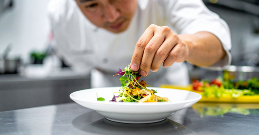 Chef plating a gourmet dish with fresh microgreens as garnish.